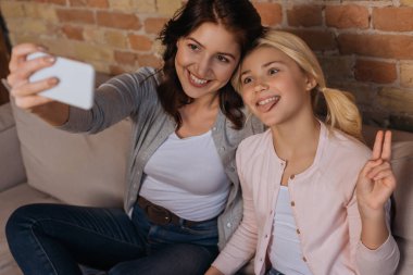 Gülümseyen annenin akıllı telefonuyla selfie çektiği seçici odak noktası. Kızının yanında huzur veren ve dilini dışarı çıkaran. 