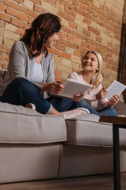 Dijital tableti kanepede tutarken annesine gülümseyen çocuğun düşük açılı görüntüsü 