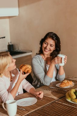 Annenin mutfakta kahvaltıda kruvasanla çocuğa gülümsediği seçmeli bir odak noktası.  
