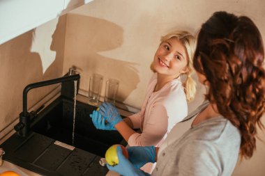 Plastik eldivenli gülümseyen çocuğun seçici odak noktası mutfakta annesinin yanında elma yıkamak. 