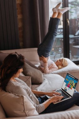 KYIV, UKRAINE - 24 Nisan 2020: Kanepede kızına yakın Amazon sitesi kullanan bir kadının seçici odak noktası 