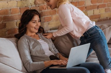 Gülümseyen kız, evde bilgisayarla çalışan annesine dokunuyor.