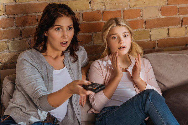 Selective focus of excited mother and daughter watching movie at home 