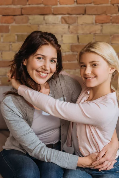 Sonrientes Madre Hija Mirando Cámara Mientras Abraza Sofá —  Fotos de Stock