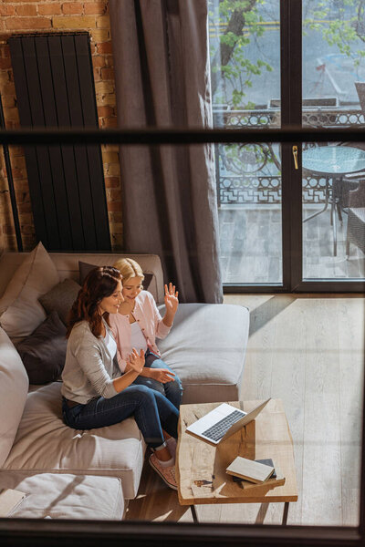High angle view of positive mother and kid having video chat on laptop in living room