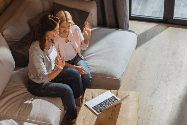 High angle view of positive kid and mother having video call on laptop in living room