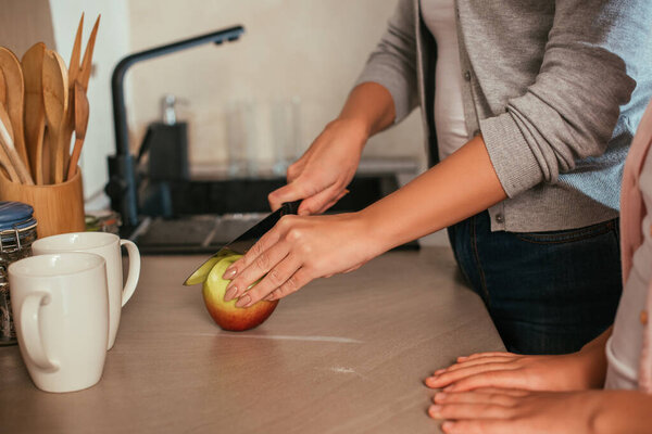 Cropped view of mother and daughter cutting fresh apple on kitchen worktop 