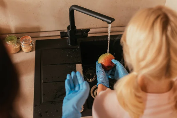 乳胶手套中孩子在母亲身边清洗苹果的选择性焦点 — 图库照片