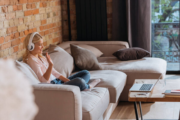 Side view of cheerful child in headphones having video call on laptop in living room