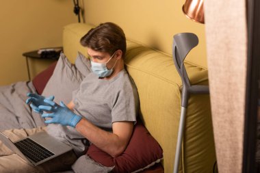 Medikal maskeli engelli bir adamın laptopuyla yatakta görüntülü konuşma yapması. 