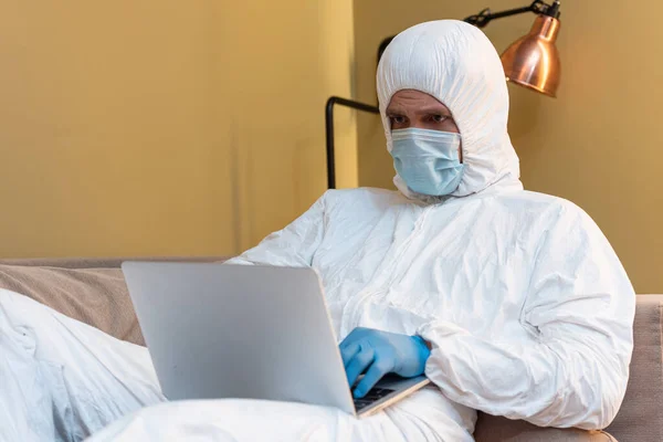 Focalizarea Selectivă Omului Masca Medicală Costumul Hazmat Folosind Laptopul Canapea — Fotografie, imagine de stoc