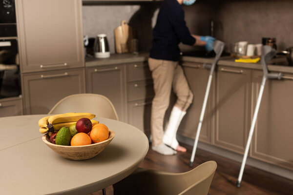 Selective focus of fruits on table and man with broken leg washing hands 