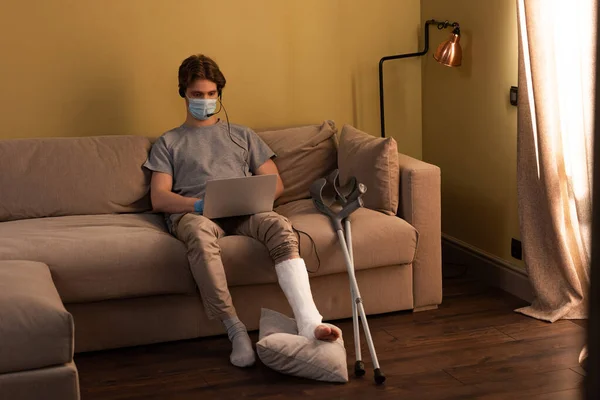 Hombre Con Máscara Médica Con Pierna Rota Usando Auriculares Mientras — Foto de Stock