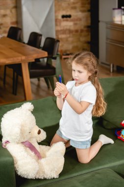 Doktorculuk oynarken oyuncak şırıngayı oyuncak ayının yanında tutan sevimli çocuk. 