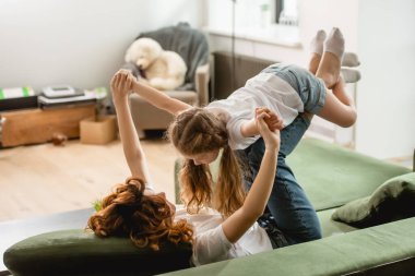 Kıvırcık anne kanepede uzanıyor, tatlı çocuğu kaldırıyor ve oturma odasında el ele tutuşuyor. 