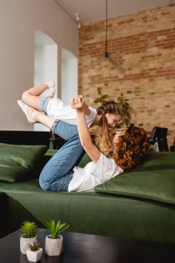 Kıvırcık annenin seçici odak noktası kanepeye uzanmış, kızını kaldırıyor ve el ele tutuşuyor. 