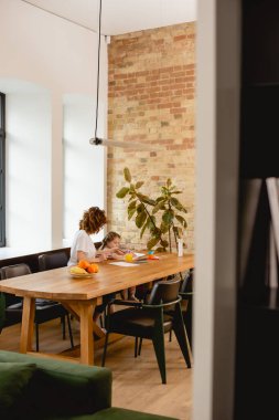 Kızının yanında oturan kıvırcık annenin seçici odağı ve evde meyveler