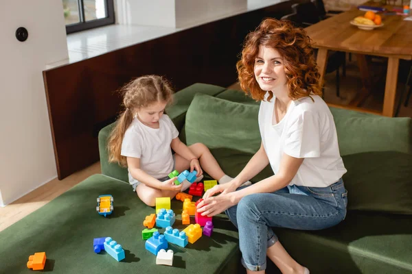 卷曲的母亲笑着靠近女儿 在客厅里玩积木游戏 — 图库照片