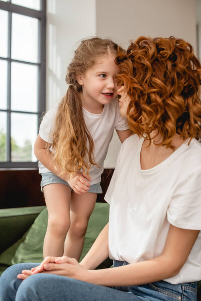 cute kid looking at curly mother sitting on sofa