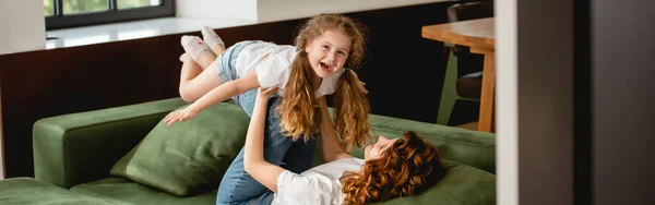 Panoramic Orientation Curly Mother Lying Sofa Lifting Happy Daughter Holding — Stock Photo, Image