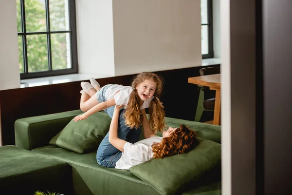 Selective Focus Curly Mother Lying Sofa Lifting Happy Daughter Holding — Stock Photo, Image