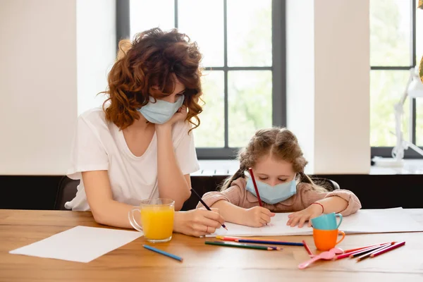 家で娘と一緒に絵を描く医療用マスクの母親 — ストック写真