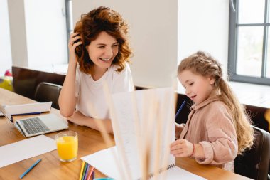 Çocuğun ve bilgisayarın yanında gülümseyen kıvırcık annenin seçici odağı 