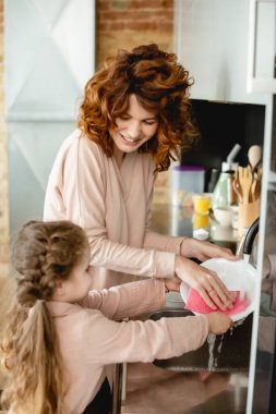 Mutlu anne ve kızın evde bulaşık yıkama odağı. 