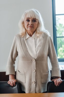 Yalnız, yaşlı bir kadın kendini izole ederken masada duruyor.