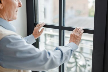 cropped view of senior lonely man looking through window on self isolation clipart