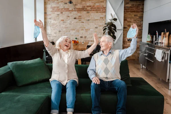 Excited Senior Couple Holding Medical Masks Sofa Quarantine — Stock Photo, Image