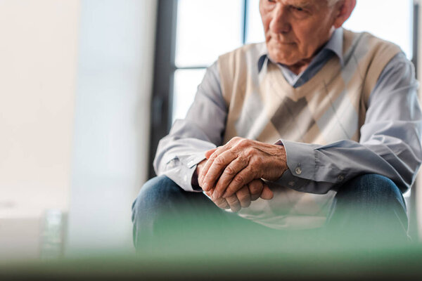 sad senior man sitting alone on sofa during self isolation, selective focus