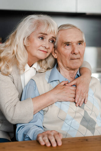 sad senior wife and husband hugging and sitting at home on quarantine