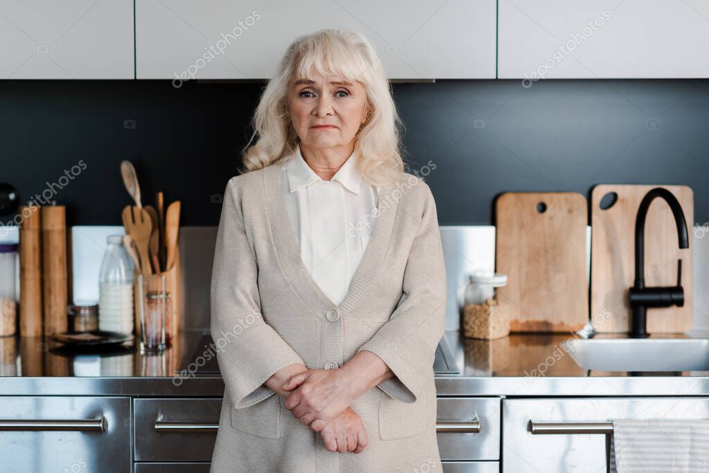 Sad senior woman standing at kitchen during self isolation