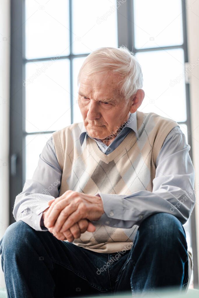 upset senior man sitting alone on sofa during self isolation