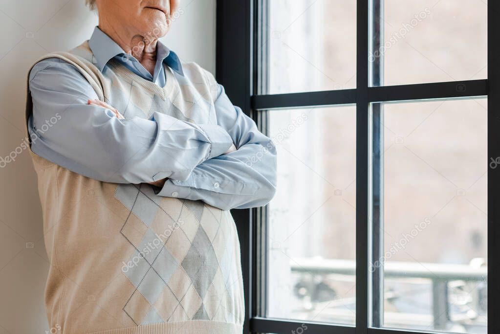 cropped view of lonely man with crossed arms standing near window during quarantine