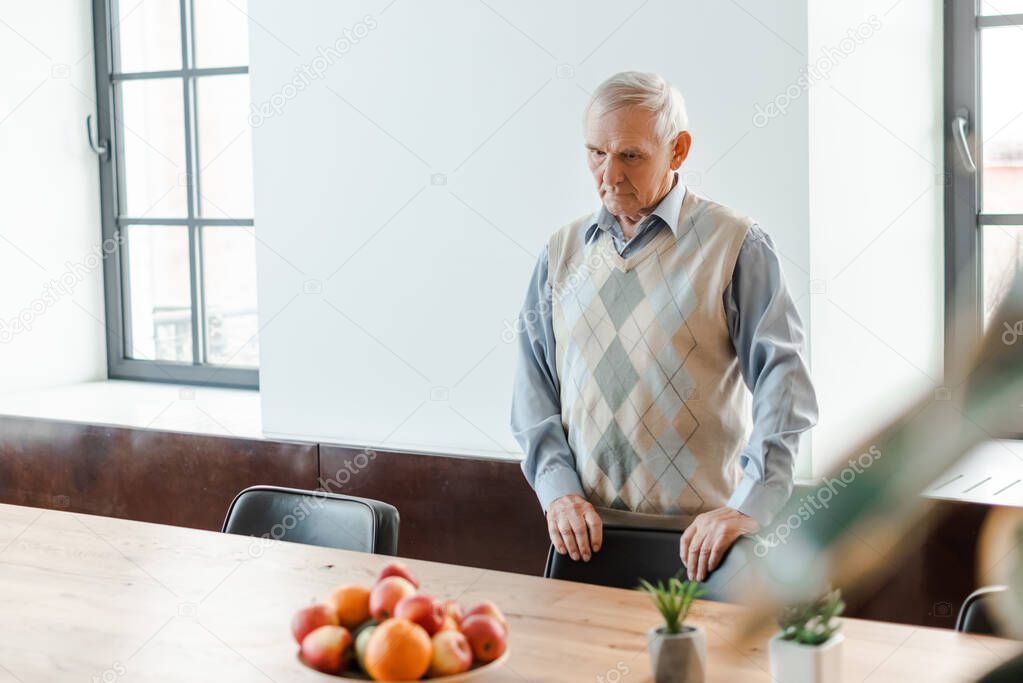lonely senior man standing at table with fruits during quarantine 