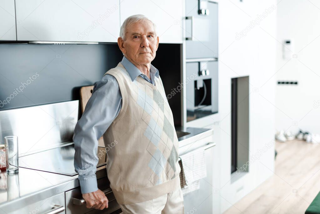 sad elderly man standing on kitchen during self isolation 