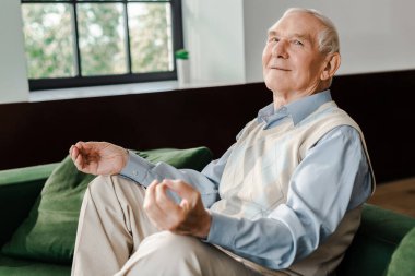 Mutlu, yaşlı bir adam, evdeki kanepede kendini izole ederken meditasyon yapıyor.