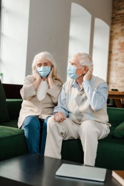 Koronavirüs salgını sırasında koltukta otururken baş ağrısı çeken yaşlı bir kadın ve koca. 