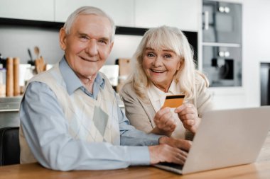 Karantina sırasında evde kredi kartı ve laptopla online alışveriş yapan mutlu yaşlı çift.