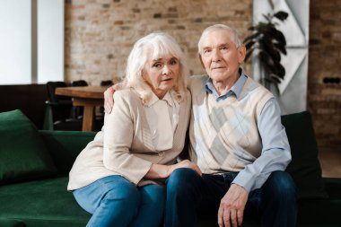 Üzgün yaşlı çift, yalnız kaldıkları sırada kanepede kucaklaşıyorlar.