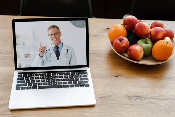 ノートパソコンを閉じて笑顔の医者が果物をテーブルの上に置いて — ストック写真