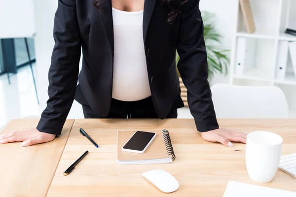 Mujer de negocios embarazada apoyada en el escritorio - foto de stock