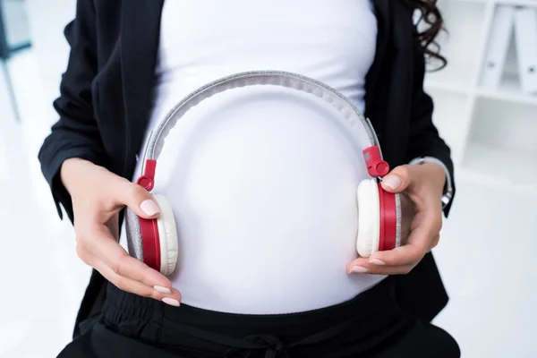 Pregnant businesswoman with headphones on tummy — Stock Photo