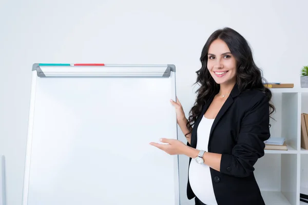 Pregnant businesswoman pointing at blank whiteboard — Stock Photo