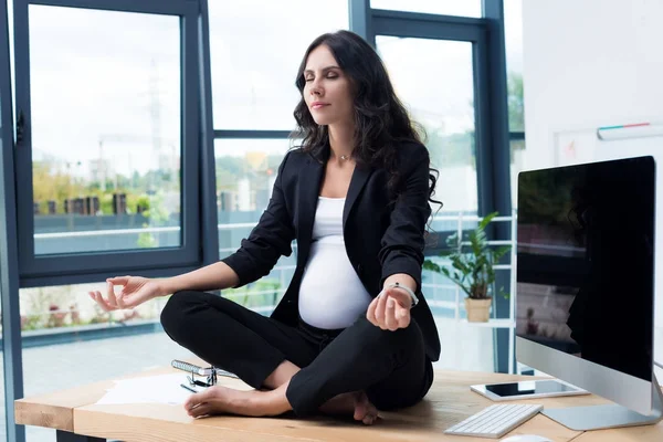 Pregnant businesswoman on table in lotus pose — Stock Photo