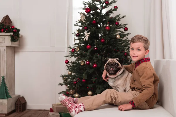 Menino sentado no sofá com pug — Fotografia de Stock