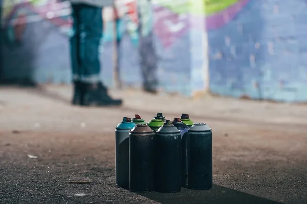 Low section of street artist painting graffiti at night, cans with aerosol paint on foreground — Stock Photo