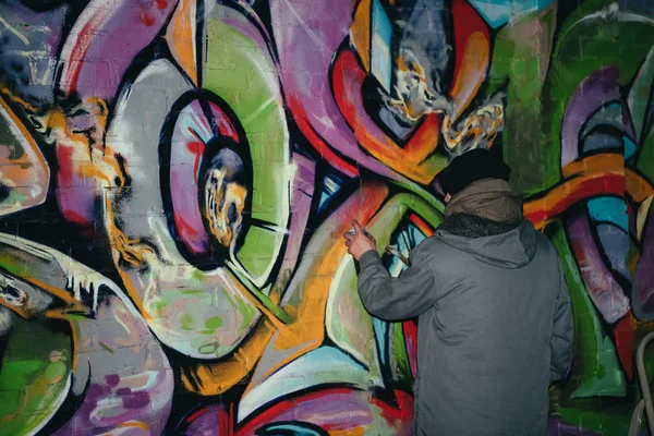 Back view of street artist painting graffiti with aerosol paint on wall at night — Stock Photo